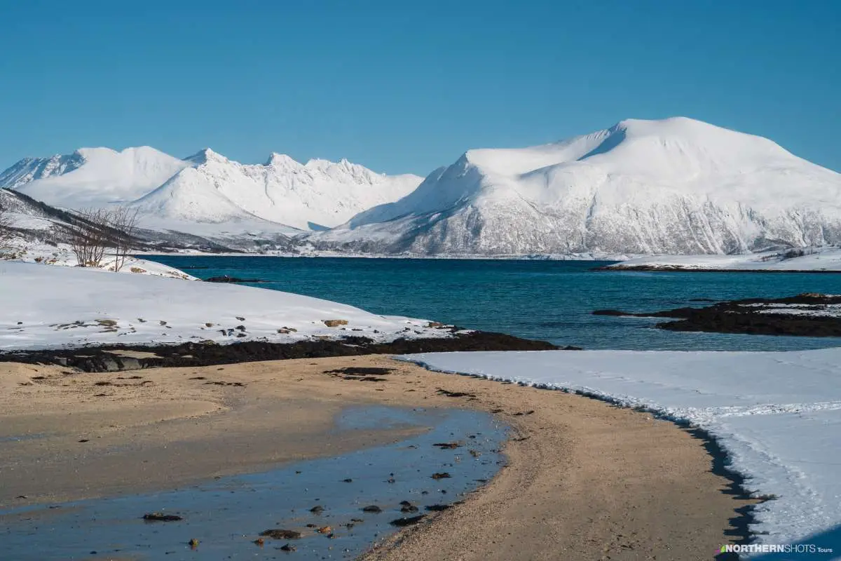 The contrasting yellow beaches of Sommarøy against their snow covered environment with the fjord and massive mountains of Vasstrand in the background.