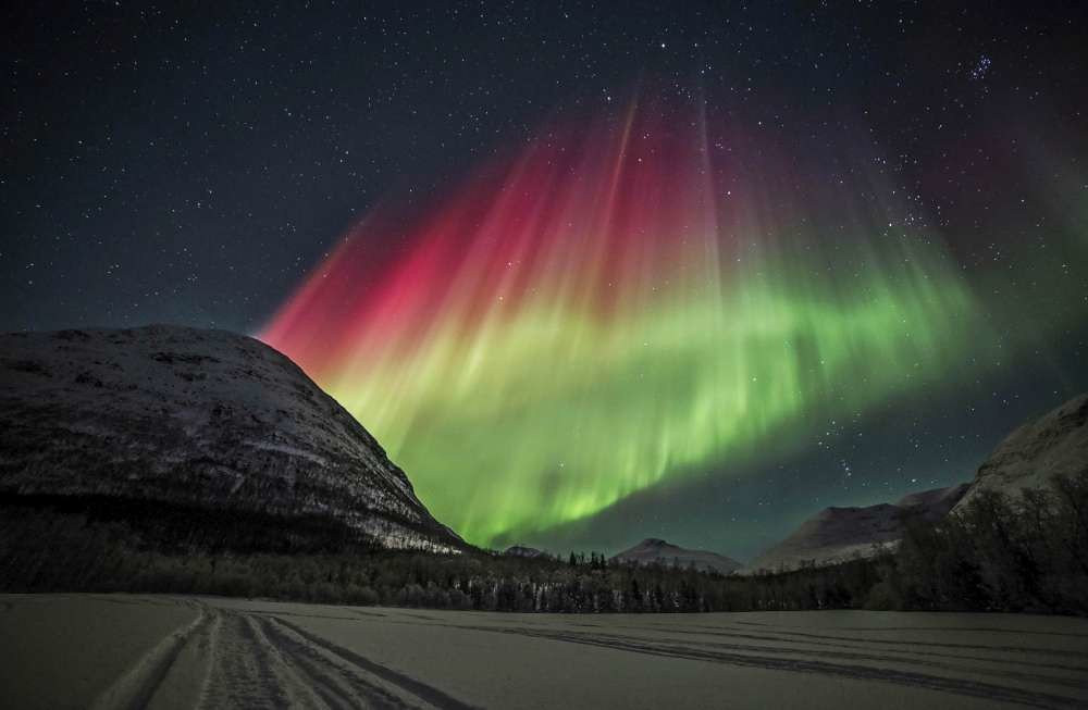 Multi-coloured curtains of Northern Lights rise from behind a snowy mountain near Tromsø in the Arctic night.