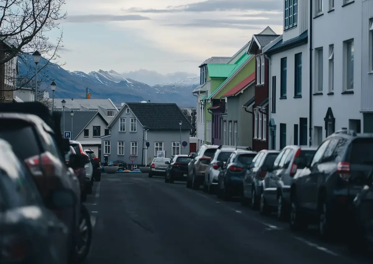 Urban backstreet in Tromsø with rows of parked vehicles, captured at night under full daylight skies.